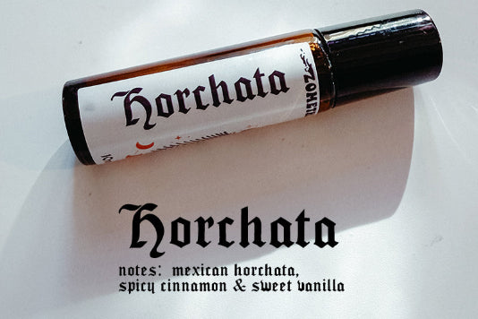 A small cylindrical roll-on bottle labeled 'Horchata' with a black cap, placed diagonally on a white surface. Below the bottle, the word 'Horchata' appears again with notes reading 'notes: mexican horchata, spicy cinnamon & sweet vanilla'.