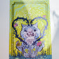 A square art print featuring a whimsical illustration of a blue-gray cat with a flower-patterned shirt, surrounded by vines and pink flowers on a bright yellow-green background, photographed against a white wall.