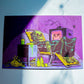 A square art print or card featuring a psychedelic horror illustration of a skeleton reclining in a chair next to a television, with neon purple, yellow, green, and black colors, photographed on a light surface with strong diagonal shadows.