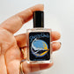 Hand holding a perfume bottle labeled 'Sleeping Whale' against a light background